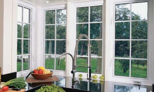 View of trees and greenery through kitchen windows, with fruits and vegetables including green onions, tomatoes, lettuce, and squash in the forefront.